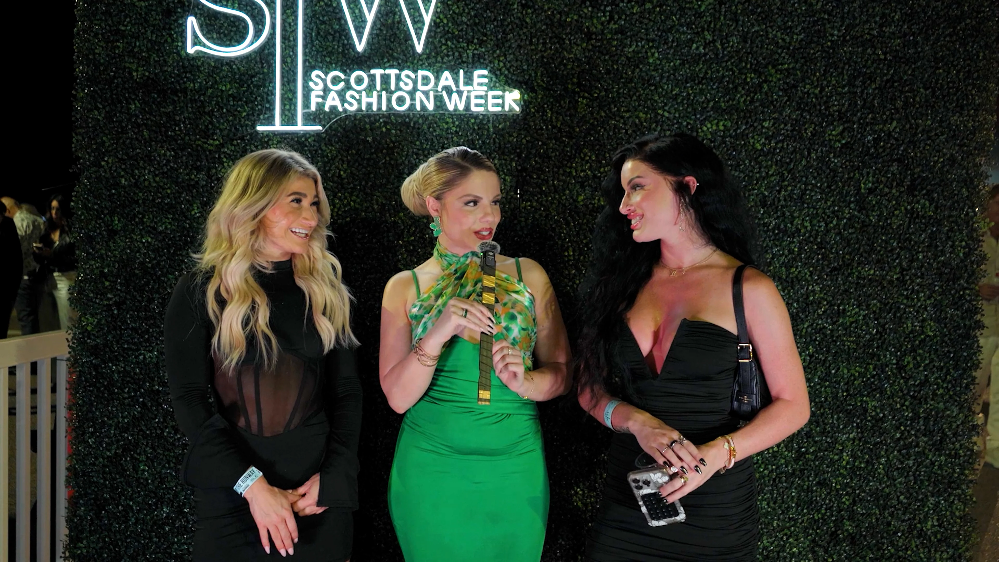 Haute Shots host conducting a red carpet interview in front of the Scottsdale Fashion Week sign.